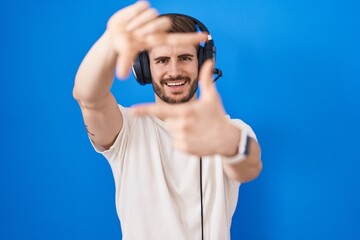 Naklejka premium Hispanic man with beard listening to music wearing headphones smiling making frame with hands and fingers with happy face. creativity and photography concept.
