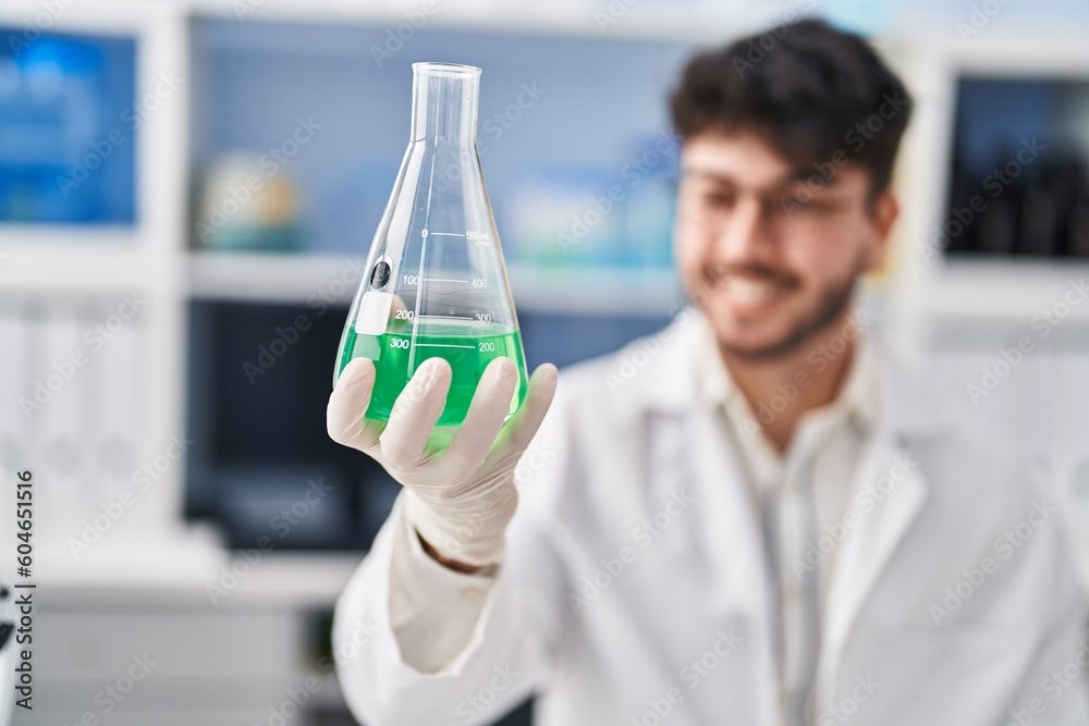 Sticker young hispanic man scientist smiling confident measuring liquid at laboratory