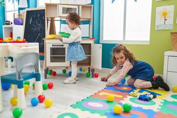 Adorable girls playing with play kitchen and car toy at kindergarten