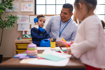 Hispanic man with boy and girl playing telephone toy standing at kindergarten