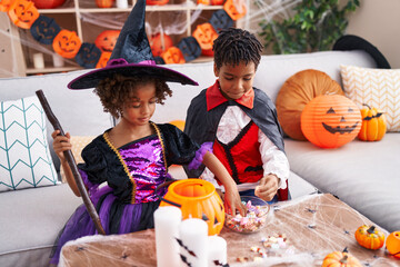 Fototapeta premium Adorable african american boy and girl wearing halloween costume holding candies of bowl at home