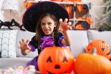Adorable hispanic girl having halloween party doing scare gesture at home