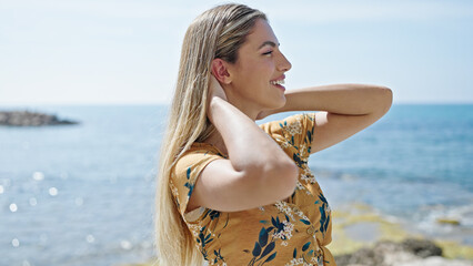 Fototapeta na wymiar Young blonde woman smiling confident combing hair at seaside