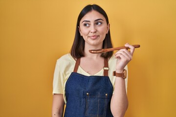 Hispanic girl eating healthy  wooden spoon smiling looking to the side and staring away thinking.