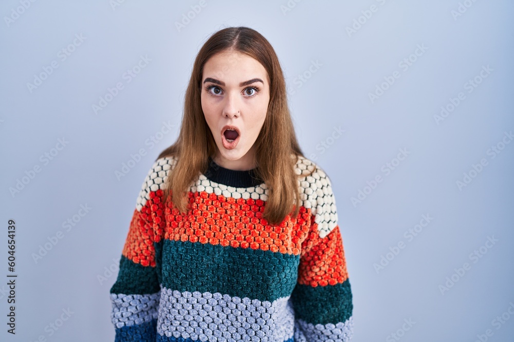 Sticker young hispanic girl standing over blue background afraid and shocked with surprise and amazed expres