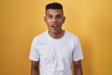 Young hispanic man standing over yellow background afraid and shocked with surprise and amazed expression, fear and excited face.