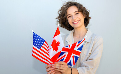 Smiling student woman hold Canada, UK and US flags and looking camera on gray wall background. English language education.