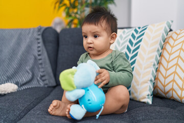 Adorable hispanic boy sitting on sofa holding elephant toy at home