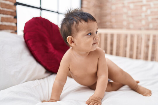 Adorable hispanic boy sitting on bed at bedroom