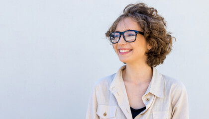 Profile portrait, smiling brunette young woman wearing glasses standing over gray wall background looking to side. © A Stock Studio