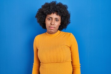 Fototapeta na wymiar Black woman with curly hair standing over blue background relaxed with serious expression on face. simple and natural looking at the camera.