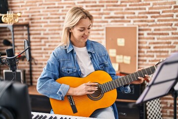 Fototapeta na wymiar Young blonde woman musician singing song playing spanish guitar at music studio