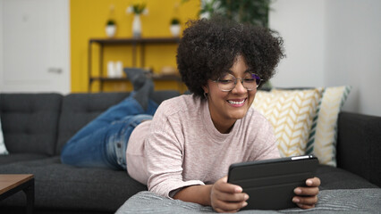Young african american woman using touchpad lying on sofa at home