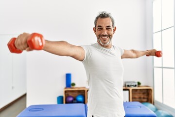 Obraz premium Middle age grey-haired man patient having rehab using dumbbells at rehab clinic