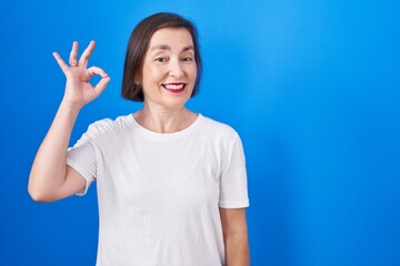 Fototapeta premium Middle age hispanic woman standing over blue background smiling positive doing ok sign with hand and fingers. successful expression.