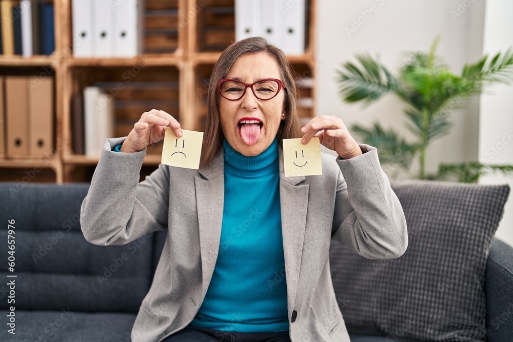 Poster middle age hispanic woman working on depression holding sad to happy emotion paper sticking tongue o