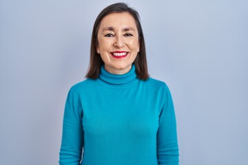 Middle age hispanic woman standing over isolated background with a happy and cool smile on face....