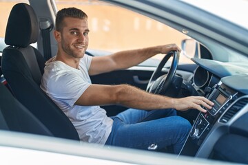 Young caucasian man sitting on car turning on radio at street