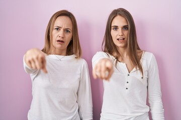 Middle age mother and young daughter standing over pink background pointing displeased and frustrated to the camera, angry and furious with you