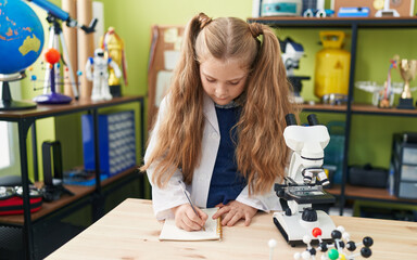 Fototapeta premium Adorable blonde girl student writing notes at laboratory classroom