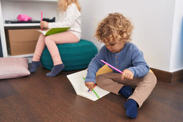 Adorable boy and girl students sitting on floor drawing on notebook at classroom