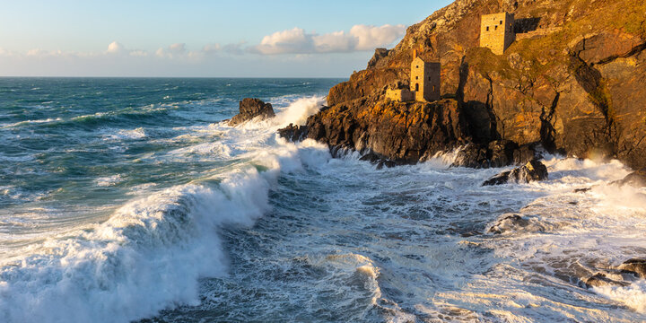 Huge, crashing winter waves strike the shore before the Crown Tin Mine engine houses, Botallack, Cornwall, England, UK
