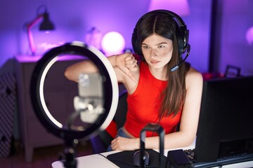 Young caucasian woman playing video games recording with smartphone with angry face, negative sign showing dislike with thumbs down, rejection concept