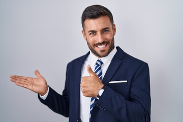 Handsome hispanic man wearing suit and tie showing palm hand and doing ok gesture with thumbs up, smiling happy and cheerful