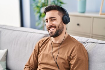 Young hispanic man listening to music sitting on sofa at home