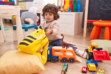 Adorable hispanic boy playing with car and dinosaur toy sitting on floor at kindergarten