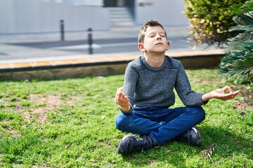 Naklejka na ściany i meble Blond child doing yoga exersice sitting on grass at park