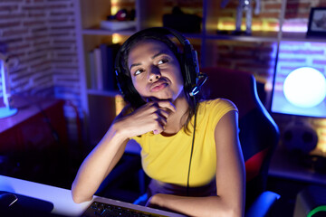 Young african american woman streamer sitting on table with doubt expression at gaming room