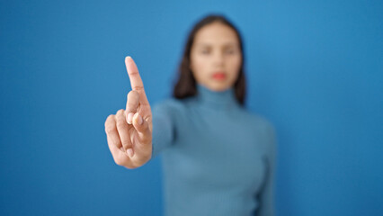 Young beautiful hispanic woman saying no with finger over isolated blue background - obrazy, fototapety, plakaty