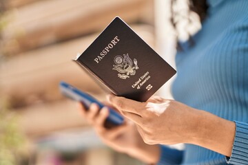 Young african american woman holding united states passport using smartphone at street