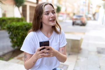 Young caucasian woman smiling confident using smartphone at street