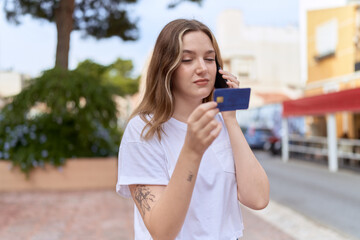 Young caucasian woman using smartphone and credit card at street