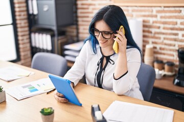 Young caucasian woman business worker using touchpad talking on smartphone at office