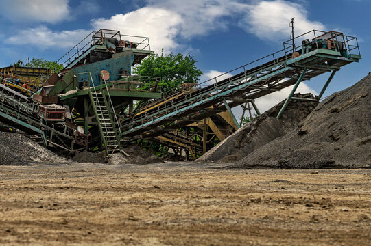 Crushing machinery, cone type rock crusher, conveying crushed granite gravel stone in a quarry open pit mining. Minning industry gravel quarry conveyor.