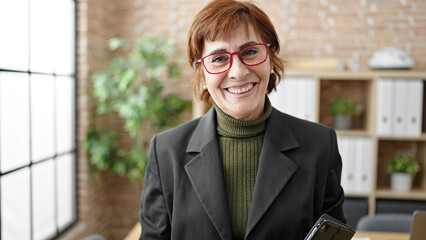 Fototapeta premium Mature hispanic woman business worker standing holding touchpad at office