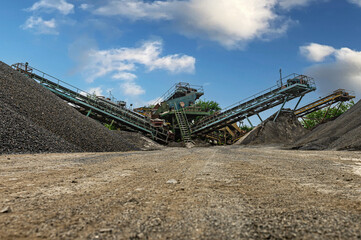 Fototapeta premium Crushing machinery, cone type rock crusher, conveying crushed granite gravel stone in a quarry open pit mining. Minning industry gravel quarry conveyor.