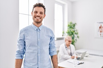 Hispanic man at doctor clinic looking positive and happy standing and smiling with a confident smile showing teeth