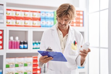 Young man pharmacist holding pills bottle reading document at pharmacy