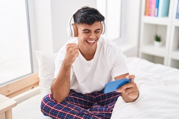 Young hispanic man smiling confident playing video game at bedroom