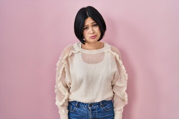 Young asian woman standing over pink background depressed and worry for distress, crying angry and...