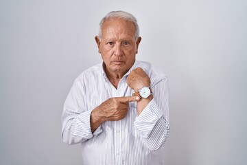 Senior man with grey hair standing over isolated background in hurry pointing to watch time,...
