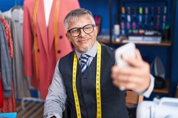Middle age grey-haired man tailor smiling confident make selfie by smartphone at clothing factory