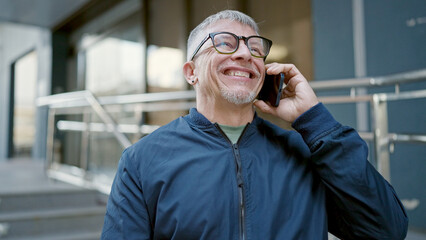 Middle age grey-haired man smiling confident talking on smartphone at street