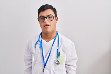 Young hispanic man with down syndrome wearing doctor uniform and stethoscope with serious expression on face. simple and natural looking at the camera.