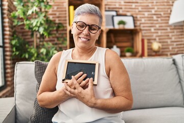 Middle age woman holding photo sitting on sofa at home