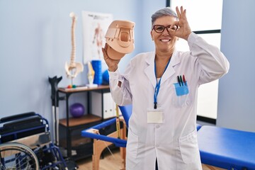 Middle age woman holding cervical neck collar smiling happy doing ok sign with hand on eye looking through fingers